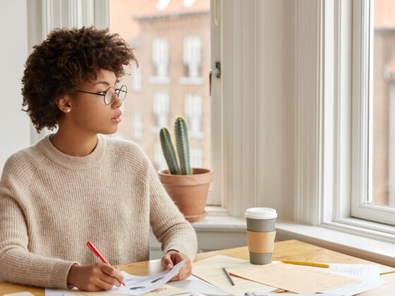 A thoughtful woman writing in her journal while gazing out the window, reflecting on her goals and God’s purpose for her in 2025