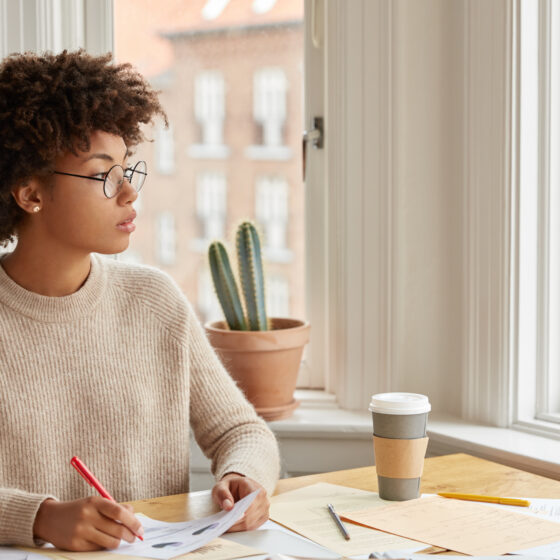A thoughtful woman writing in her journal while gazing out the window, reflecting on her goals and God’s purpose for her in 2025
