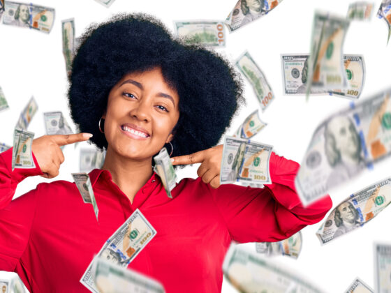 A joyful woman with her arms raised as money falls around her, symbolizing financial blessings and prosperity in 2025.
