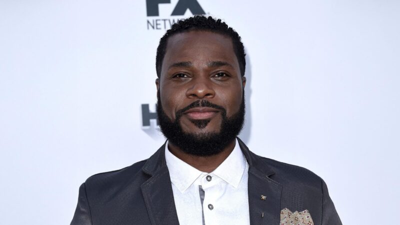 Portrait of Malcolm-Jamal Warner smiling warmly in a suit, honoring his legacy after his passing in July 2025.